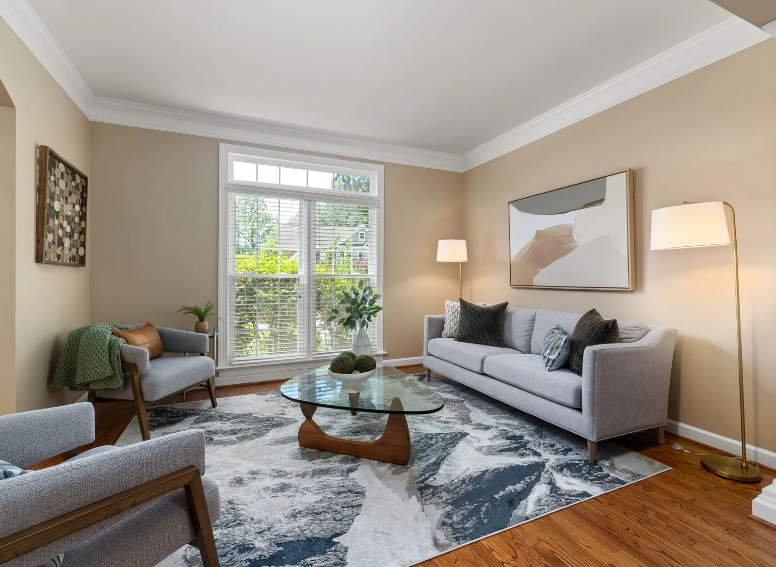 A bright, spotless living room with grey sofas, a glass coffee table on a patterned rug and tall windows